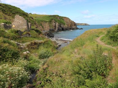 A coastal path with grassy hills and stone ruins by the sea at Carreg Yr Onnen in Penparc