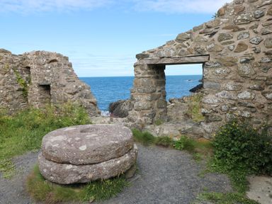 Stone ruins by the sea with a large round stone structure and rocky coastline in the background at Carreg Yr Onnen in Penparc