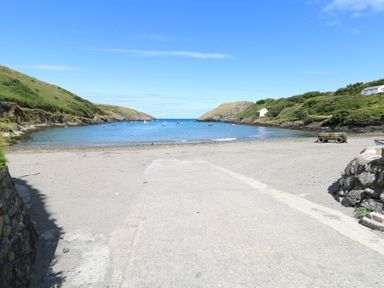 A sandy beach with a concrete boat ramp leading to a small bay with boats and green hills at Carreg Yr Onnen in Penparc