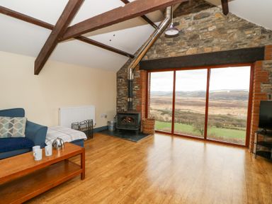 A living room with a wood stove and large windows overlooking fields at Llwyngwinau Isaf Barn in Tynreithyn near Tregaron