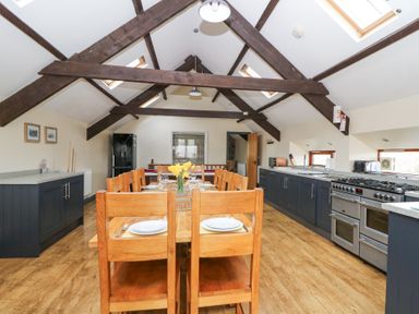 A kitchen and dining area with wooden table and chairs and exposed ceiling beams at Llwyngwinau Isaf Barn in Tynreithyn near Tregaron