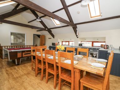 A dining area with a wooden table set for eight and a kitchen with appliances under skylights at Llwyngwinau Isaf Barn in Tynreithyn near Tregaron