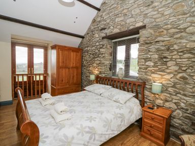 A bedroom with a wooden bed and wardrobe and stone walls at Llwyngwinau Isaf Barn in Tynreithyn near Tregaron