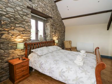 A bedroom with a wooden bed frame floral bedspread bedside table with lamp stone wall and armchair at Llwyngwinau Isaf Barn Tynreithyn near Tregaron