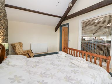 A bedroom with a wooden bed, floral patterned bedding, an armchair, and a window with blinds at Llwyngwinau Isaf Barn in Tynreithyn near Tregaron