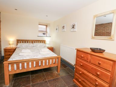 A bedroom with a wooden bed and two bedside tables with lamps a wooden dresser with a bowl a wall mirror and three floral paintings at Llwyngwinau Isaf Barn in Tynreithyn near Tregaron
