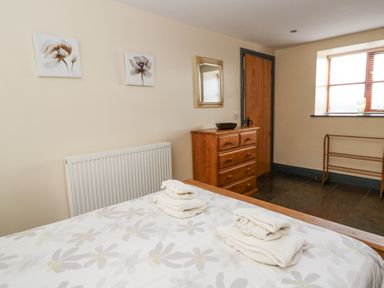 A bedroom with a bed, folded towels, wooden dresser, mirror, window, and wall art at Llwyngwinau Isaf Barn in Tynreithyn near Tregaron