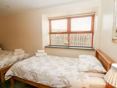 A bedroom with two single beds near a window with blinds and a small vase with flowers at Llwyngwinau Isaf Barn in Tynreithyn near Tregaron
