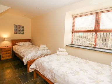 A bedroom with two single beds a wooden nightstand with a lamp a painting on the wall and a window with blinds and flowers on the sill at Llwyngwinau Isaf Barn in Tynreithyn near Tregaron