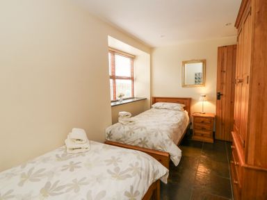 A bedroom with two single beds a wooden wardrobe and a bedside table with a lamp at Llwyngwinau Isaf Barn in Tynreithyn near Tregaron