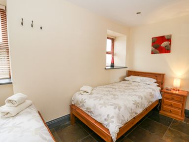A bedroom with two single beds wooden nightstand a lamp and a wall decoration at Llwyngwinau Isaf Barn in Tynreithyn near Tregaron