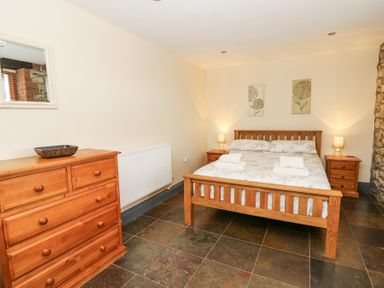 A bedroom with a wooden bed and dresser beside a stone wall at Llwyngwinau Isaf Barn in Tynreithyn near Tregaron