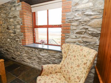A floral armchair next to a window with stone and brick walls at Llwyngwinau Isaf Barn Tynreithyn near Tregaron