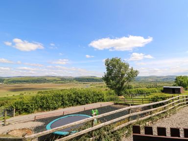 An outdoor view with a trampoline, fence, and hills at Llwyngwinau Isaf Barn in Tynreithyn near Tregaron