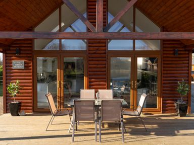 A wooden deck with a glass table and six chairs outside a cabin with glass doors at The Green Monkey in North Hykeham