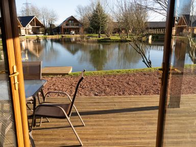 A wooden deck with chairs and table overlooking a pond with wooden houses around at The Green Monkey in North Hykeham