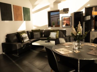 A living room with a black leather sectional sofa and a coffee table next to a dining table with placemats and flowers at The Green Monkey in North Hykeham