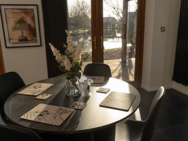 A dining table with placemats, coasters, a glass vase with flowers, and salt and pepper shakers by a glass door and a framed picture at The Green Monkey in North Hykeham