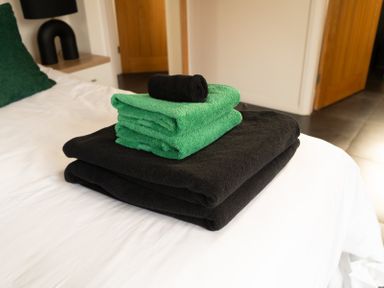 Folded black and green towels on a white bed in a bedroom at The Green Monkey in North Hykeham