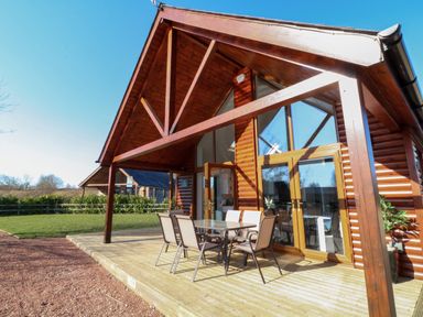 A wooden cabin with glass doors and an outdoor dining table with chairs on a deck at The Green Monkey in North Hykeham