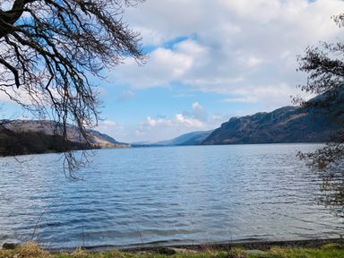 A lake with mountains in the background and tree branches framing the view at Low Wood View in Hartsop