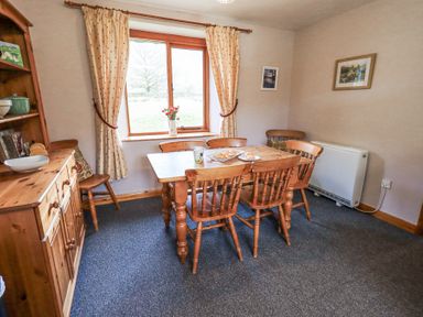 A dining room with a wooden table and chairs near a window with curtains at Low Wood View in Hartsop