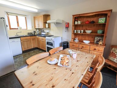 A kitchen with wooden cabinets a dining table with croissants and mugs and a wooden dresser at Low Wood View in Hartsop
