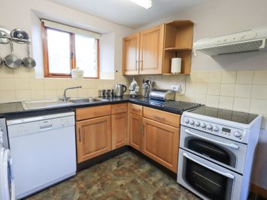 A kitchen with wooden cabinets dishwasher oven sink and cooking utensils at Low Wood View in Hartsop