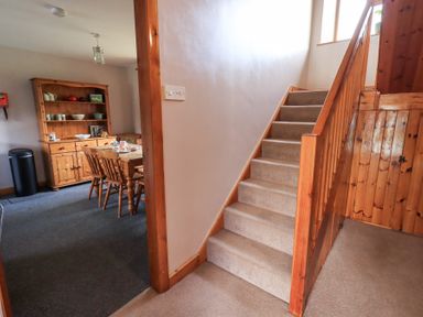 A staircase with carpet leading upstairs next to a dining room with a wooden table chairs and a cabinet at Low Wood View in Hartsop