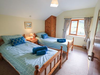A bedroom with two single beds bedside table with lamp window with curtains and wooden wardrobe at Low Wood View in Hartsop