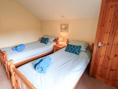 A bedroom with two single wooden beds with blue checkered bedding and blue towels at Low Wood View in Hartsop