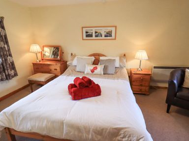 A bedroom with a double bed with red towels on it bedside tables with lamps a dressing table with a mirror a chair and curtains at Low Wood View in Hartsop