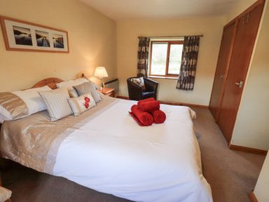 A bedroom with a bed pillows bedside table lamp chair window and double wardrobe at Low Wood View in Hartsop