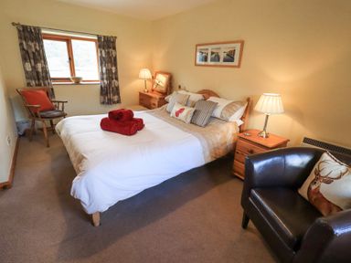 A bedroom with a double bed red towels on the bed wooden bedside tables with lamps a window wooden chair and a black armchair at Low Wood View in Hartsop