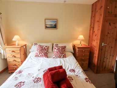 A bedroom with a double bed with red patterned pillows and red towels on it two wooden bedside tables with lamps and a wooden wardrobe at Low Wood View in Hartsop