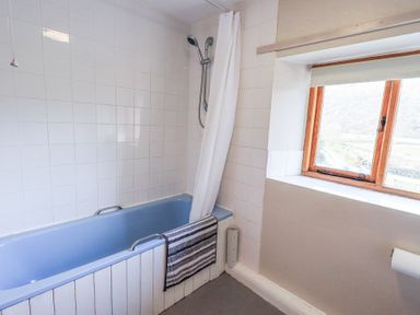 A bathroom with a blue bathtub a shower and a window at Low Wood View in Hartsop