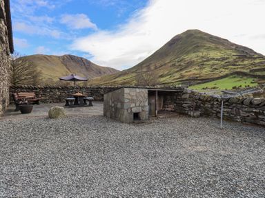 An outdoor patio area with a picnic table with umbrella a bench a stone structure dry stone walls and mountains in the background at Low Wood View in Hartsop