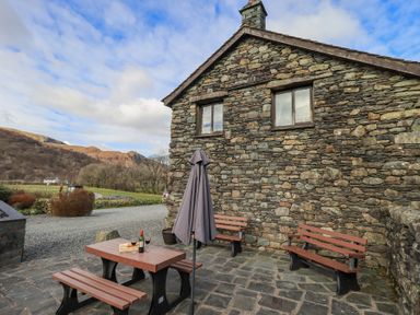 An outdoor patio with benches and a table with wine glasses and a bottle next to a stone building at Low Wood View in Hartsop