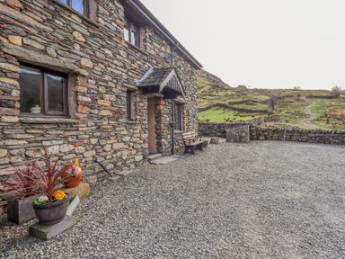 A stone house with a gravel yard flowers in pots and a bench with hills in the background at Low Wood View in Hartsop