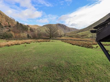 A grassy field with a stone wall and a tree in a hilly landscape under a blue sky at Low Wood View in Hartsop