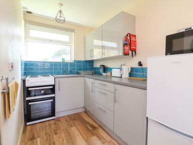 A kitchen with white cabinets blue tiled backsplash stove sink kettle and refrigerator at 24 The Glade in Kilkhampton