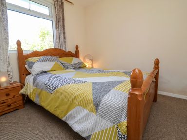 A bedroom with a wooden bed with patterned bedding a wooden nightstand and a window at 24 The Glade in Kilkhampton