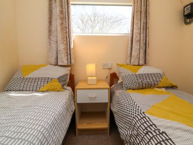 A bedroom with two single beds separated by a wooden nightstand with a lamp at 24 The Glade in Kilkhampton