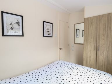 A bedroom with a bed covered in a heart patterned duvet two framed flower pictures on the wall a wooden wardrobe and a wall mirror at 31B Foxburrow Hang Fritton near Belton Norfolk