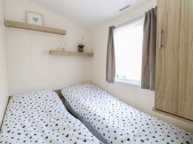 A bedroom with two beds with heart patterned bedding a window with curtains and wooden shelves at 31B Foxburrow Hang in Fritton near Belton Norfolk