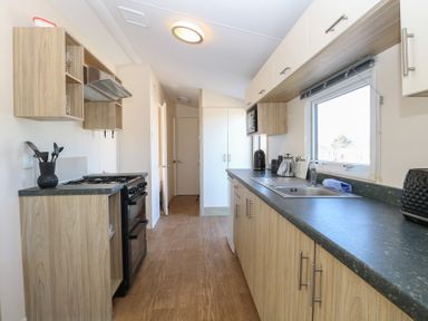A kitchen with wooden cabinets a black gas stove a sink and a window at 31B Foxburrow Hang in Fritton near Belton Norfolk