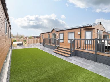 A patio area with artificial grass and wooden mobile homes at Blossom Vale Lodge in Evesham