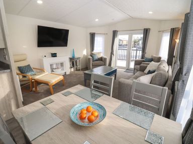 A living room with a sofa armchairs a TV and a dining table with fruit at Blossom Vale Lodge in Evesham