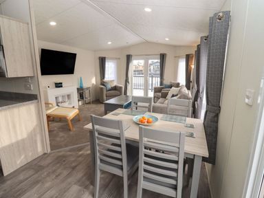 A living room and dining area with a dining table and chairs and sofas in the background at Blossom Vale Lodge in Evesham