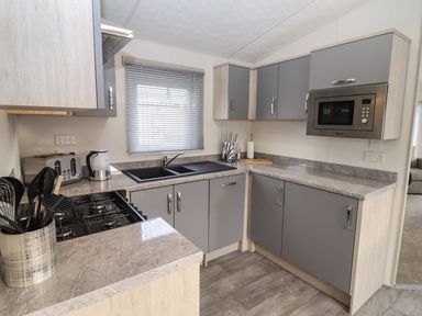 A kitchen with grey cabinets a black sink a microwave oven and kitchen utensils at Blossom Vale Lodge in Evesham